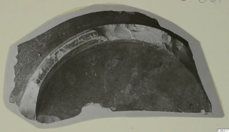 Curved pottery sherd with a dark surface and a pale band along one edge, shown on a grey card mount