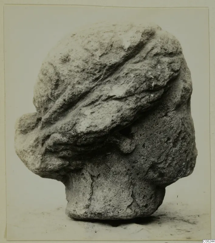 Stone head sculpture from Soli, seen from the side, with carved bands across the top of the head and worn features
