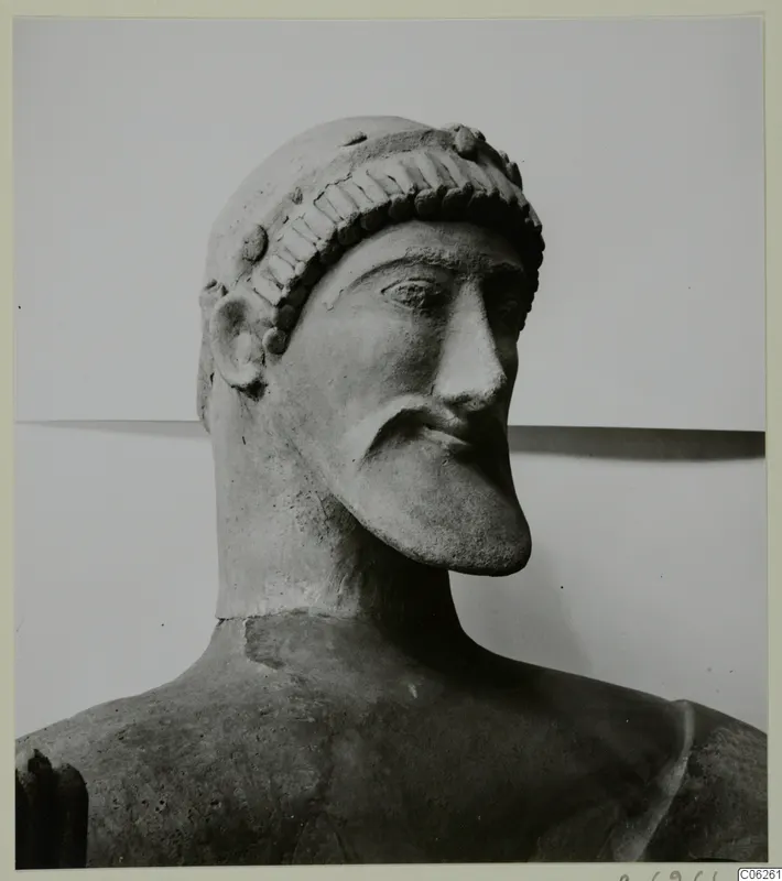 Terracotta sculpture of a bearded male head with a headband, from Mersinaki, photographed in three-quarter view.