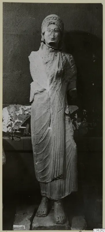 Limestone statue of a standing female figure from Vouni, in a long draped garment, shown against a dark background.