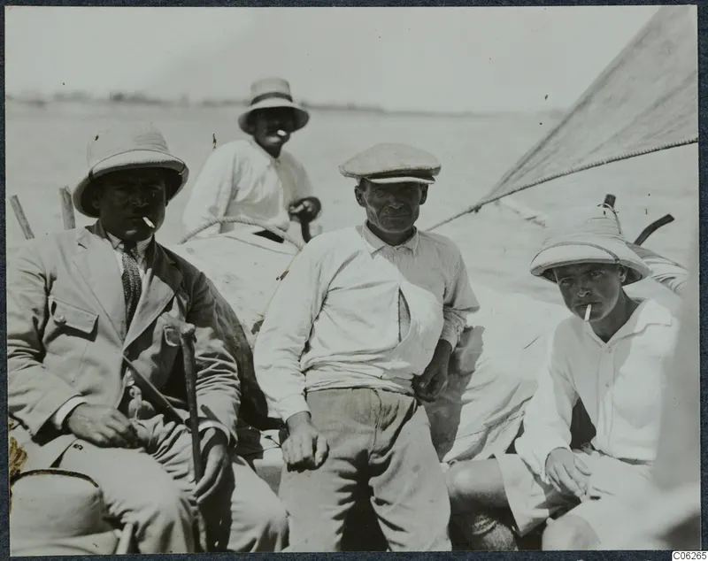 Four men seated in a small sailing boat at Baghazi, with a sail rising at the right edge.