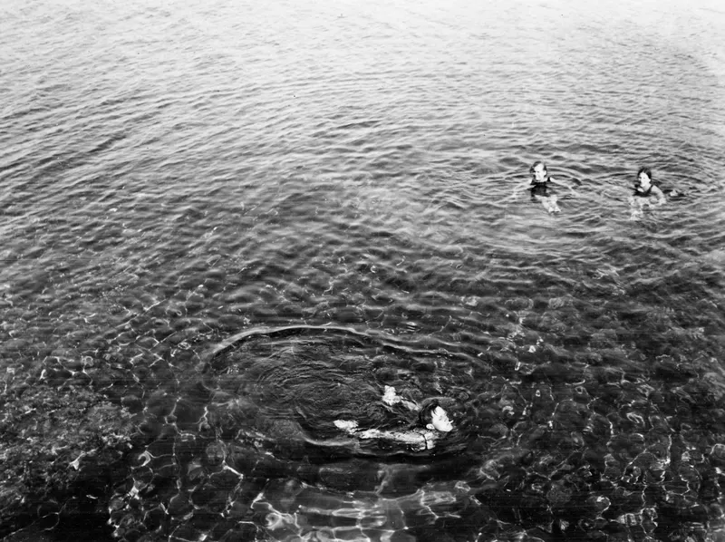 Three people swimming in clear sea water at Kyrenia, seen from above.