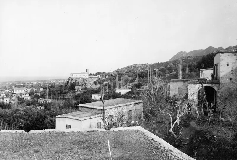 View from the village of Lapithos over white houses, a whitewashed church on a rocky knoll, and hills beyond.