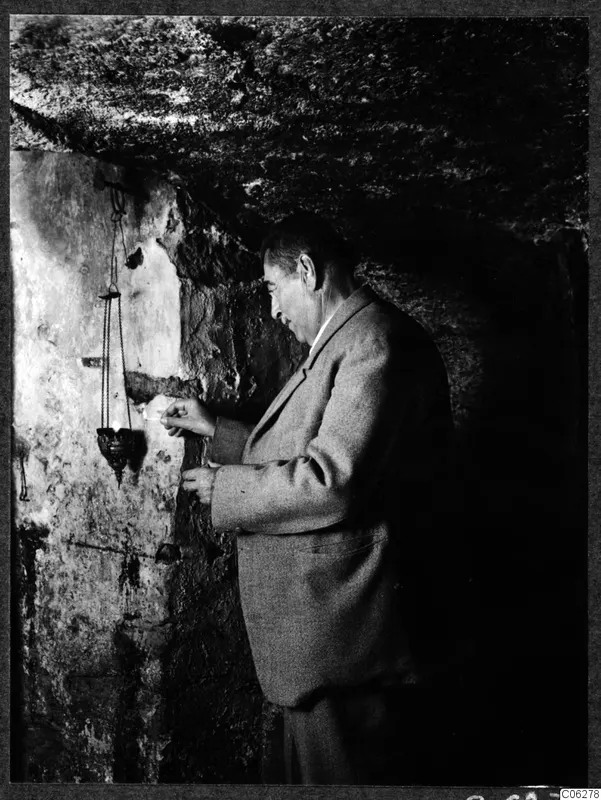Perides lighting a hanging lamp in a stone chamber at Kition, Larnaca