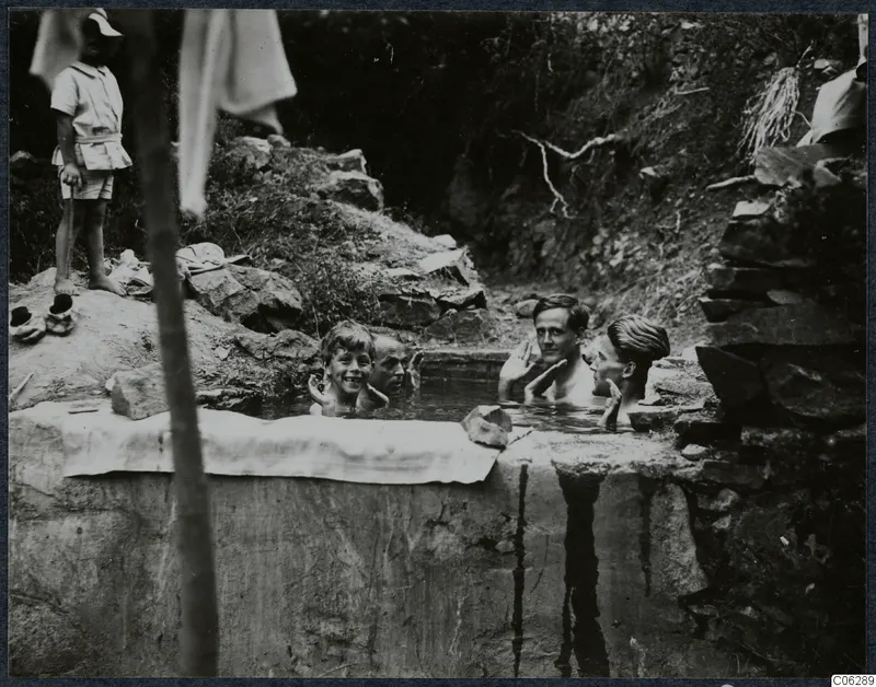 Four people bathing in a stone-lined cistern at Machairas, with a boy standing on the bank.