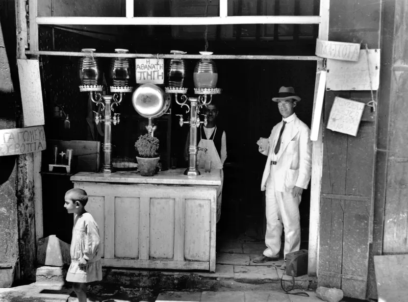 Juice stall in Nicosia with glass dispensers on a counter, and a man in a light suit standing in the doorway.