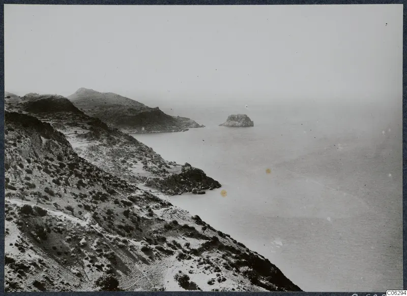 Rocky coastline with scrub-covered slopes falling to the sea, with a small rocky islet offshore.