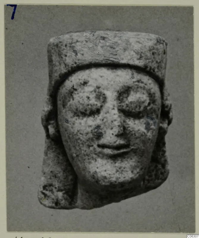 Limestone head from Kition with large eyes and a flat-topped cylindrical headdress.
