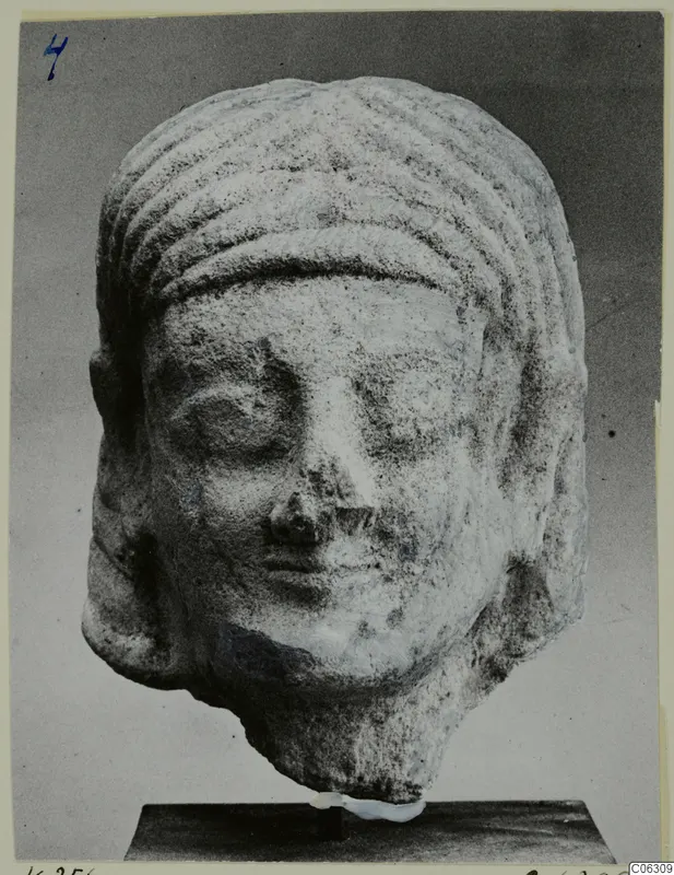 Limestone head sculpture from Kition, with ridged hair bands and lowered eyes, shown on a dark stand