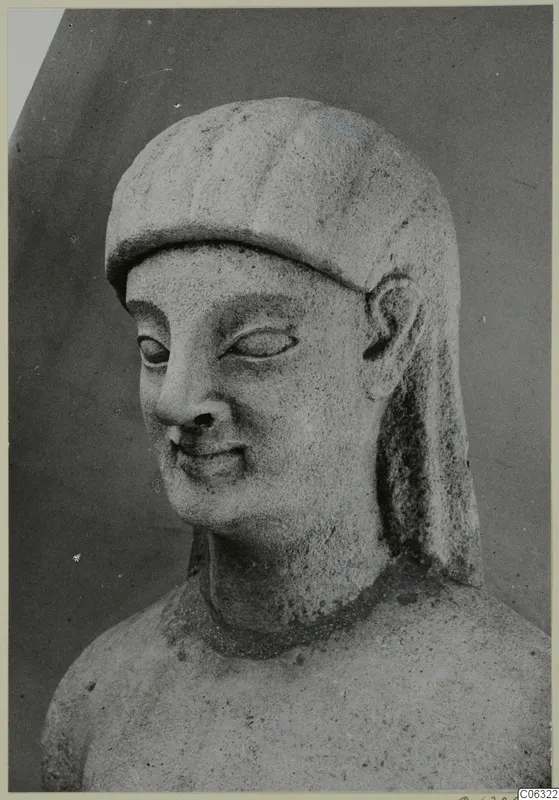 Limestone head from Kition, turned slightly to one side, with a close-fitting head covering and a faint smile.