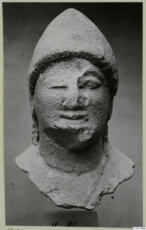 Limestone head fragment from Kition with a tall pointed cap, shown frontally on a small block base