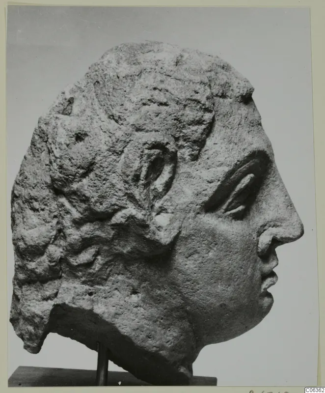 Carved stone head from Mersinaki, shown in profile facing right on a wooden stand.