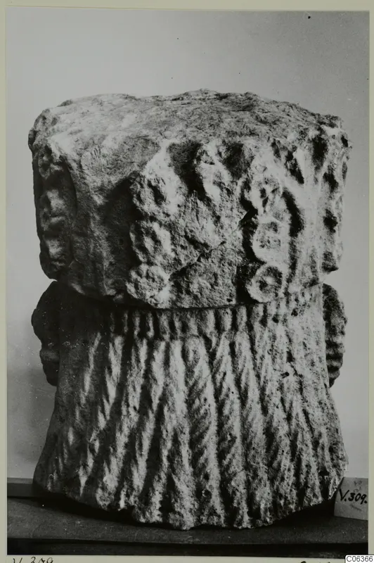 Carved limestone fragment with rounded relief on its upper part and vertical ridges below, shown on a table against a grey backdrop.