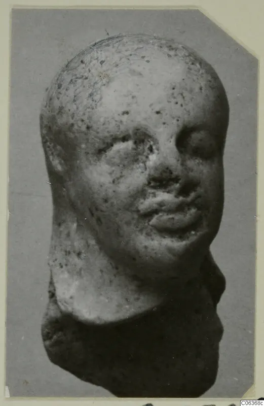Terracotta figurine head from Vouni, photographed against a grey background