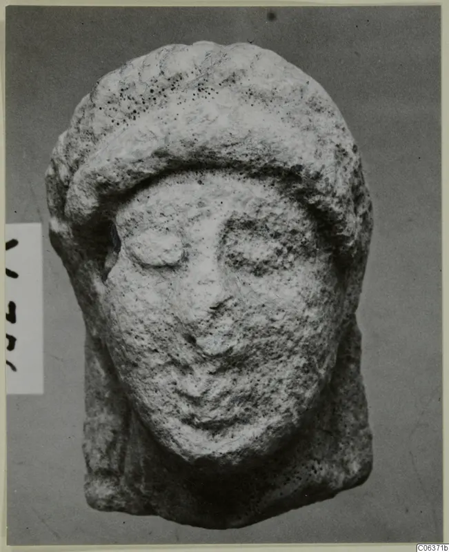Limestone head from Vouni, seen from the front, with a band across the forehead and a pitted surface.