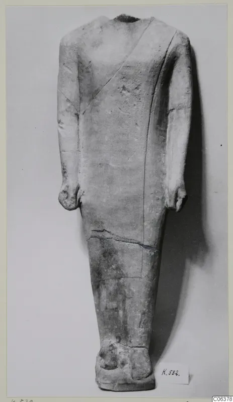 Headless limestone standing statue with arms held at its sides, shown against a plain grey background.
