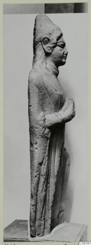 Limestone standing figure from Vouni, seen in profile on a plinth against a plain grey backdrop.