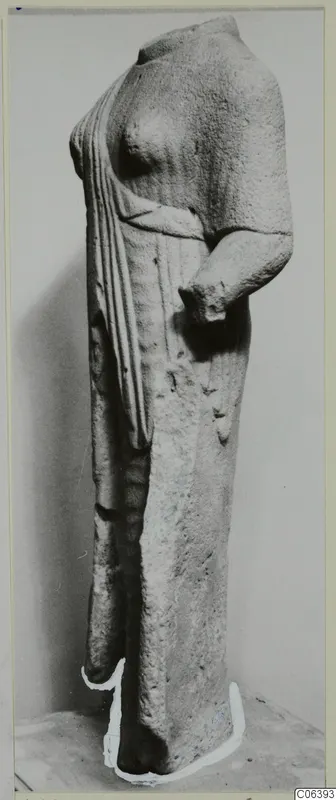 Headless limestone statue of a standing figure in a long garment, photographed against a grey backdrop
