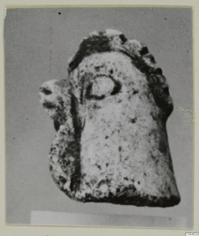 Small limestone figurine fragment with a rounded, head-like top and a projection on the left side.