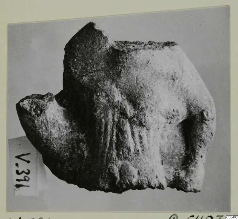 Broken figurine fragment from Vouni with a rough, worn surface, shown on a plain grey backdrop.