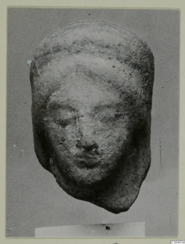 Terracotta head of a figure from Vouni, shown frontally against a plain grey backdrop