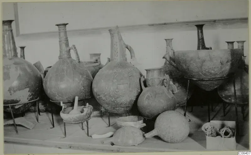 Several large jugs, a bowl and a round flask with patterned surfaces, displayed on metal stands in a museum room.