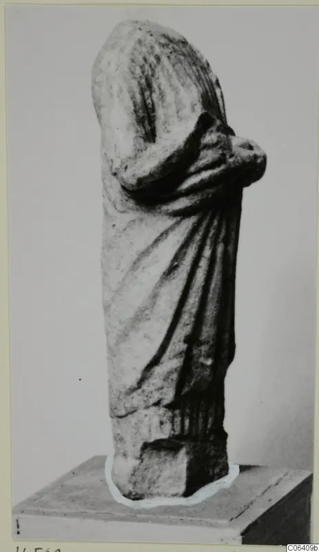 Limestone statue of a draped standing figure from Vouni, head missing, arms folded across the chest, shown on a plinth