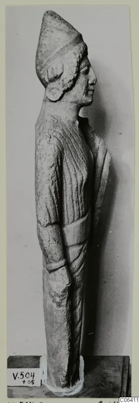 Limestone standing figure in side profile from Vouni, wearing a tall cap, shown on a dark base