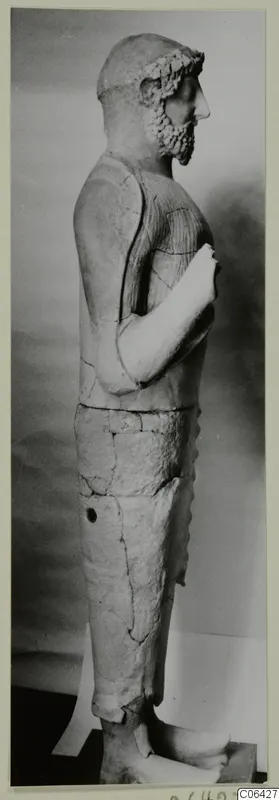 Terracotta statue of a standing bearded man, seen in side profile on a dark base