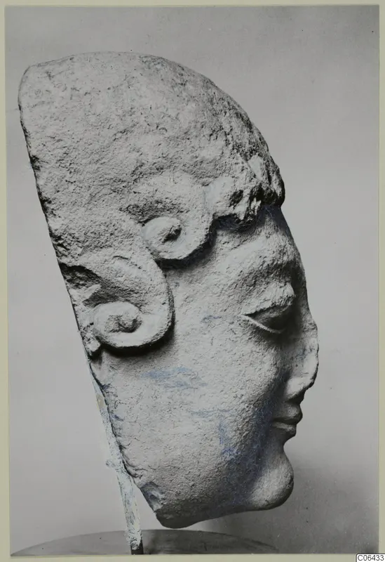 Limestone sculpture of a head from Arsos, with a high hair mass and spiral curls at the side.