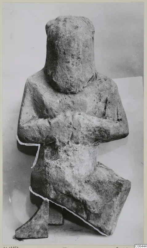 Limestone sculpture of a seated figure with arms folded across the body, head rounded and featureless