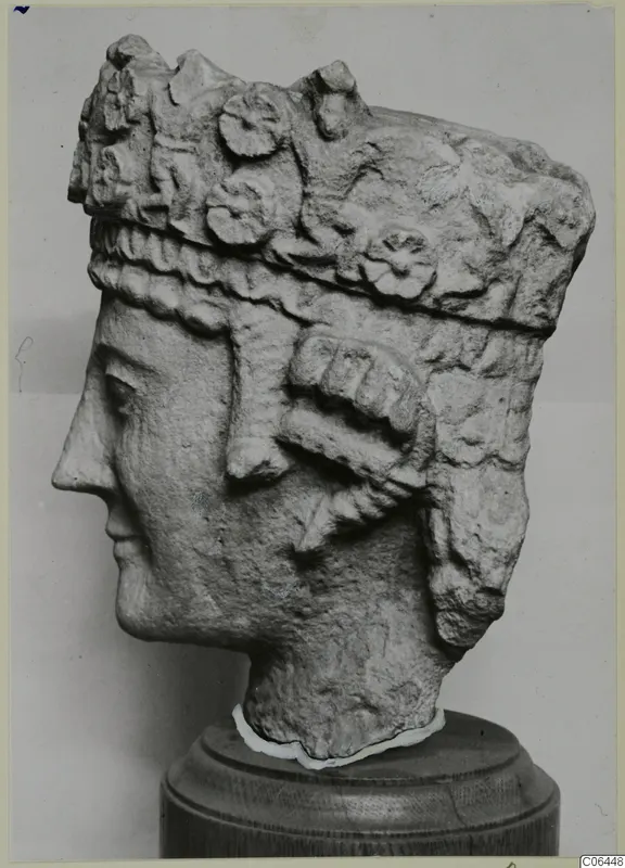 Carved limestone head in profile with a tall decorated headdress, on a wooden stand, from Vouni