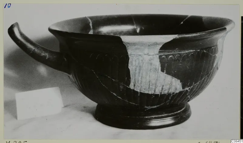 Black-glazed kylix with a single curved handle and vertical ribbing on the lower body