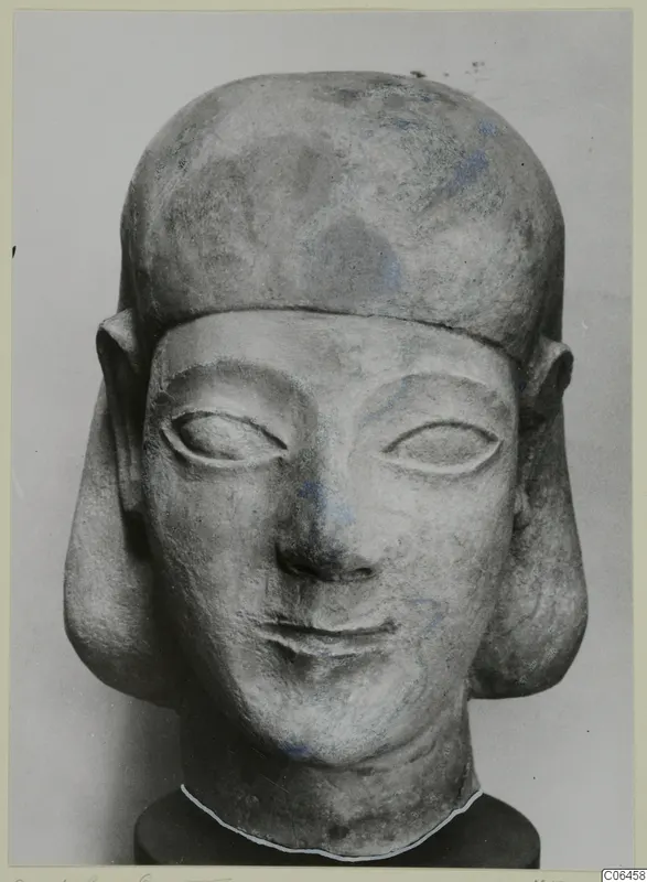 Limestone sculpture head with a flat-topped headdress, large ears and traces of blue paint, photographed from the front