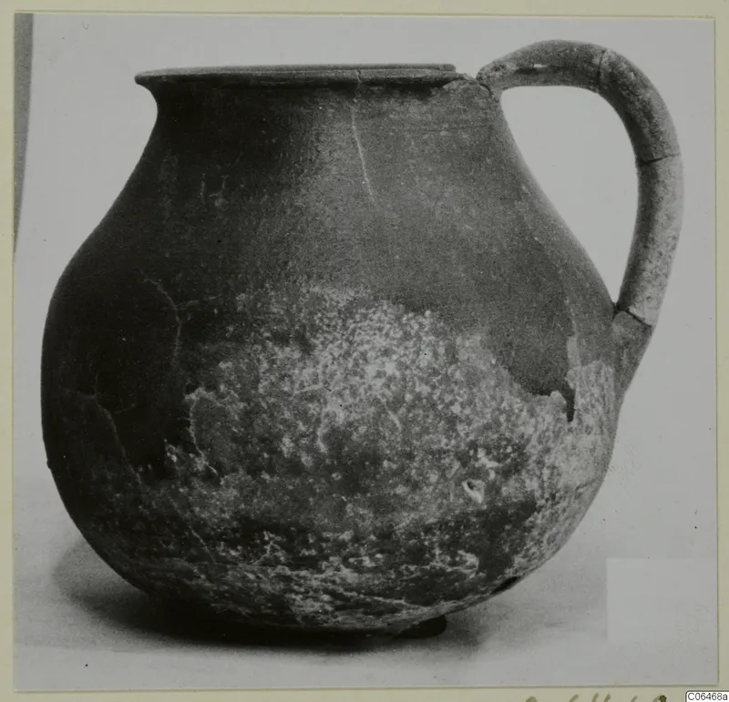 Coarse ware jug with a rounded body, flat rim and strap handle, photographed against a pale background.