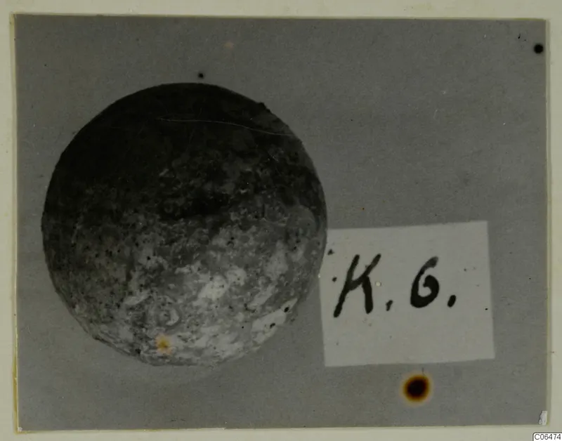 Round, pitted object photographed beside a small handwritten label card, Kition collection photograph