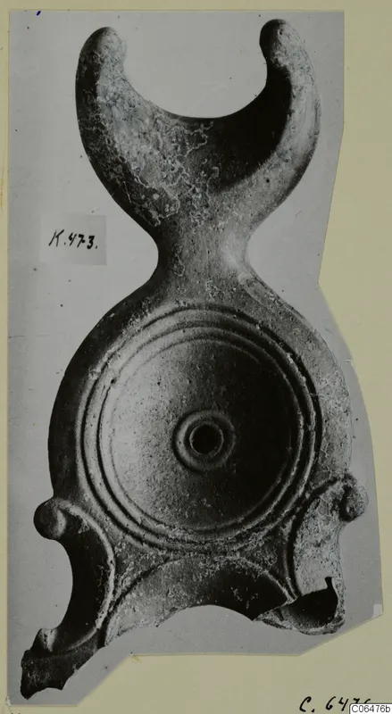 Terracotta lamp seen from above, with concentric grooves on its round disc and a crescent-shaped handle with two knobbed ends