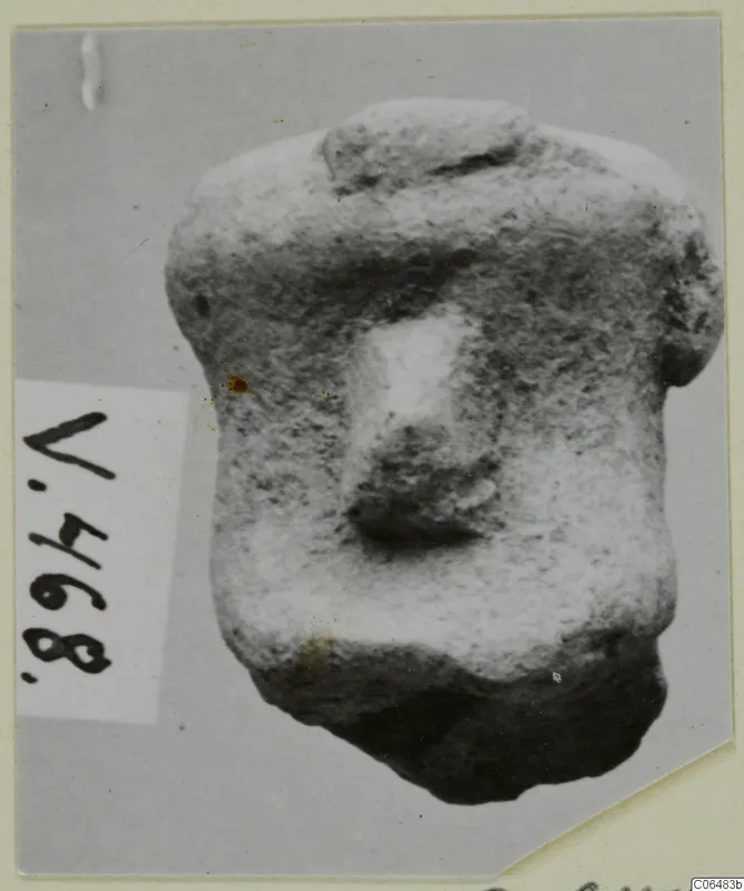 Terracotta figurine fragment with a blocky body and a rounded projection at the centre, shown on a grey card mount beside a number label