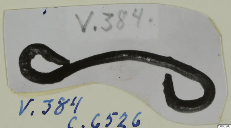 Dark metal rod with a loop at one end and a hook at the other, photographed on a card mount, from Vouni