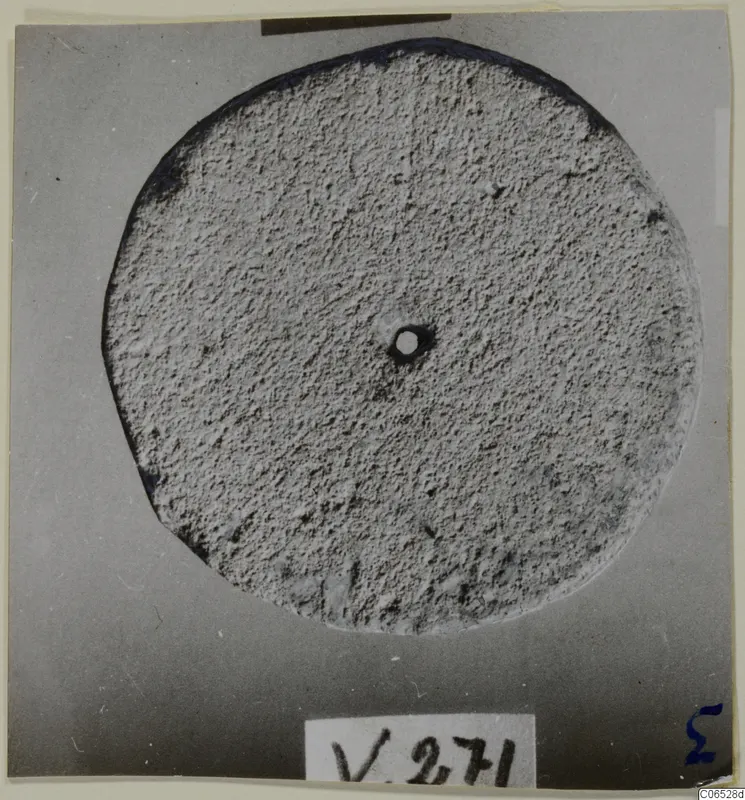 Round flat stone disc with a small central hole, photographed from above against a grey backdrop.