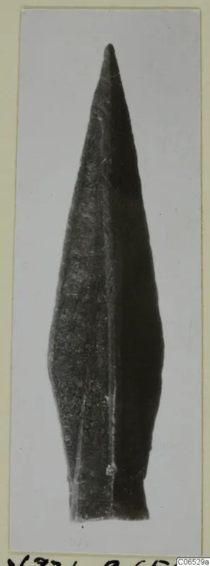 Leaf-shaped metal arrowhead from Vouni, photographed upright against a pale card.