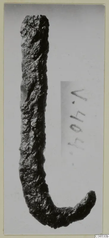 Corroded iron hook with a long straight shank and a short curved end, photographed against a grey background