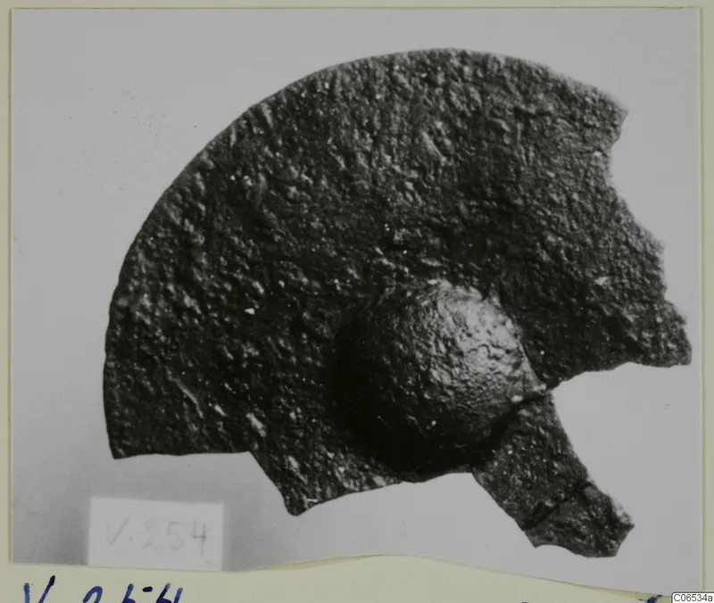 Corroded bronze mounting fragment from Vouni with a rounded knob, photographed on a pale ground.