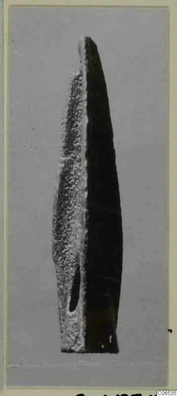 Long pointed metal blade, probably a weapon, with an oval hole near its base, shown upright on a grey backdrop.