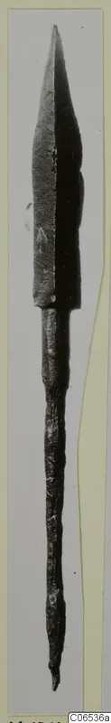 Bronze arrowhead from Vouni with a long tang, photographed upright against a pale grey background.