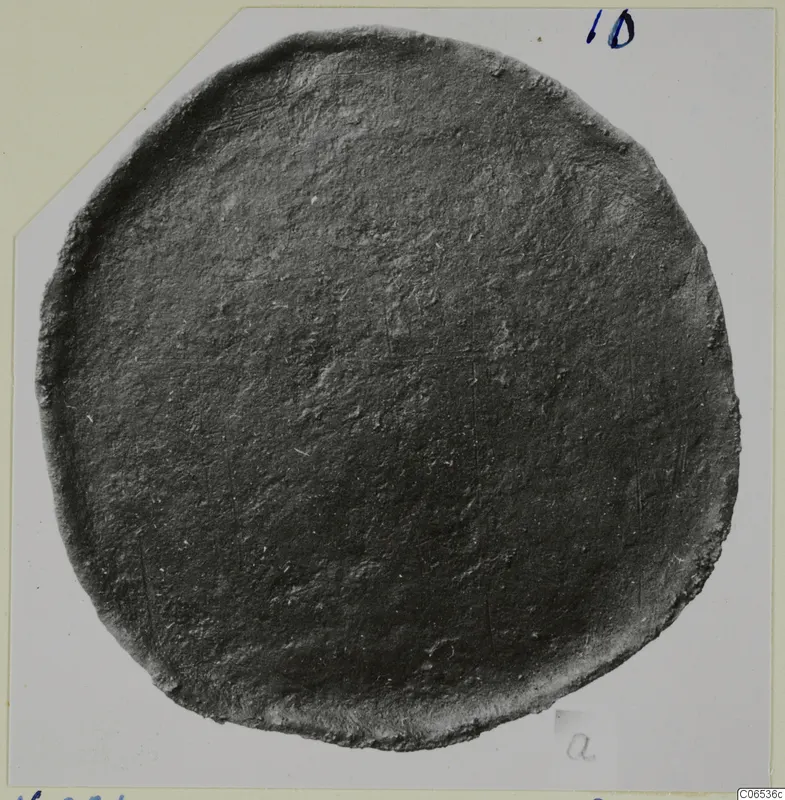 Disc-shaped bronze fragment from Vouni with a raised rim and dark, corroded surface