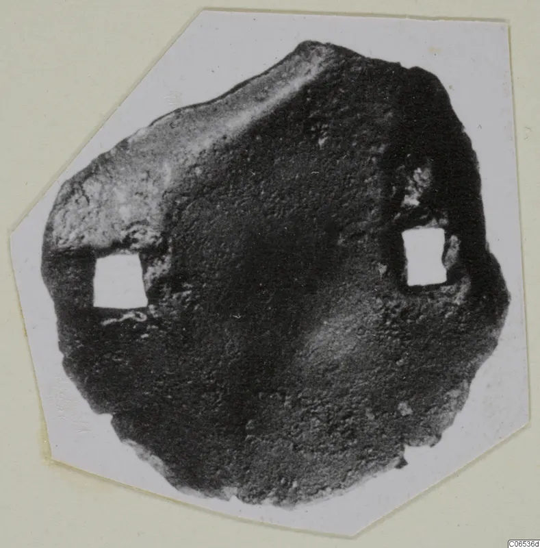 Corroded bronze mounting fragment from Vouni with two square openings, shown on a pale card mount
