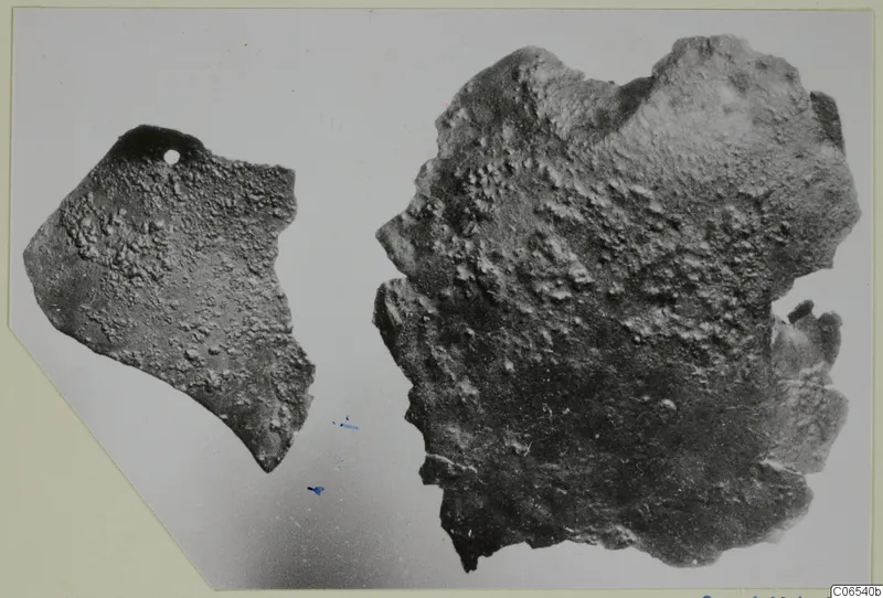 Two corroded bronze fragments from Vouni, one smaller piece with a small hole near its top edge