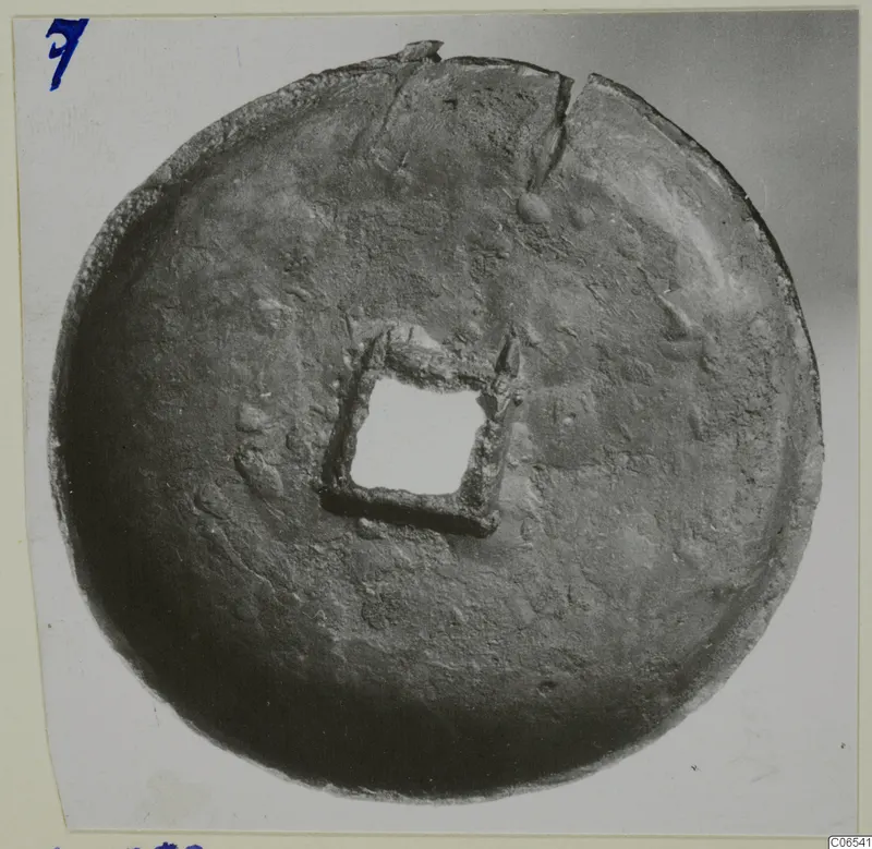 Round metal disc with a square central opening framed by a square metal mount, cracked at the top edge
