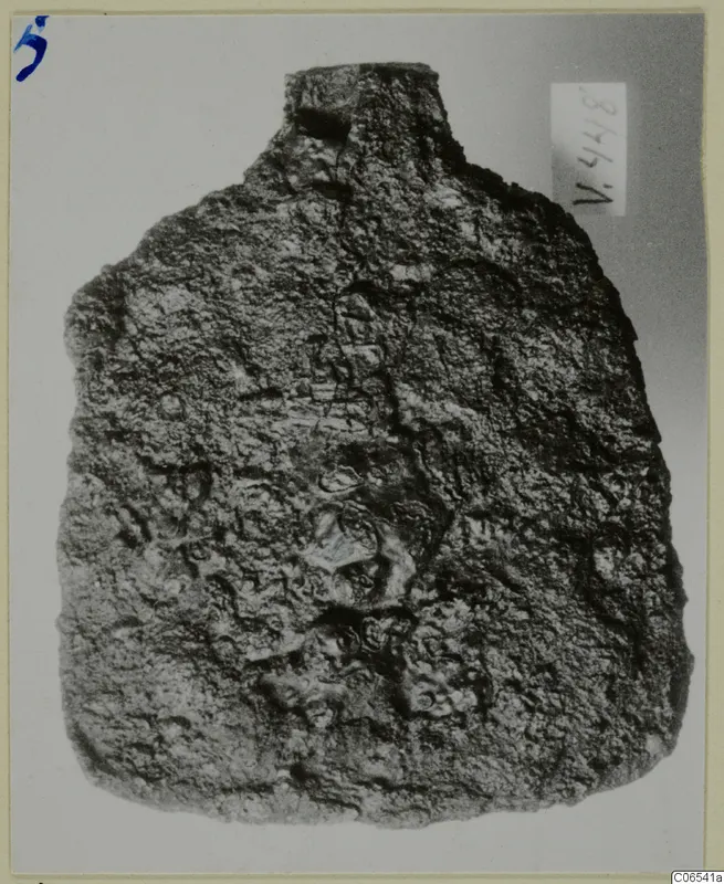 Corroded iron tool, possibly a spade, from Vouni, shown upright against a pale grey background.